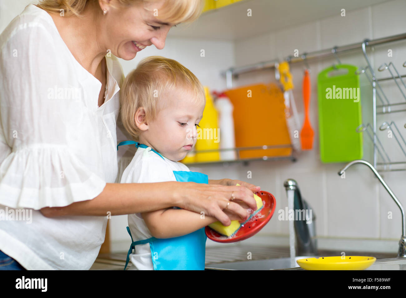 Kid boy and mother washing dishes - having fun together in the kitchen Stock Photo