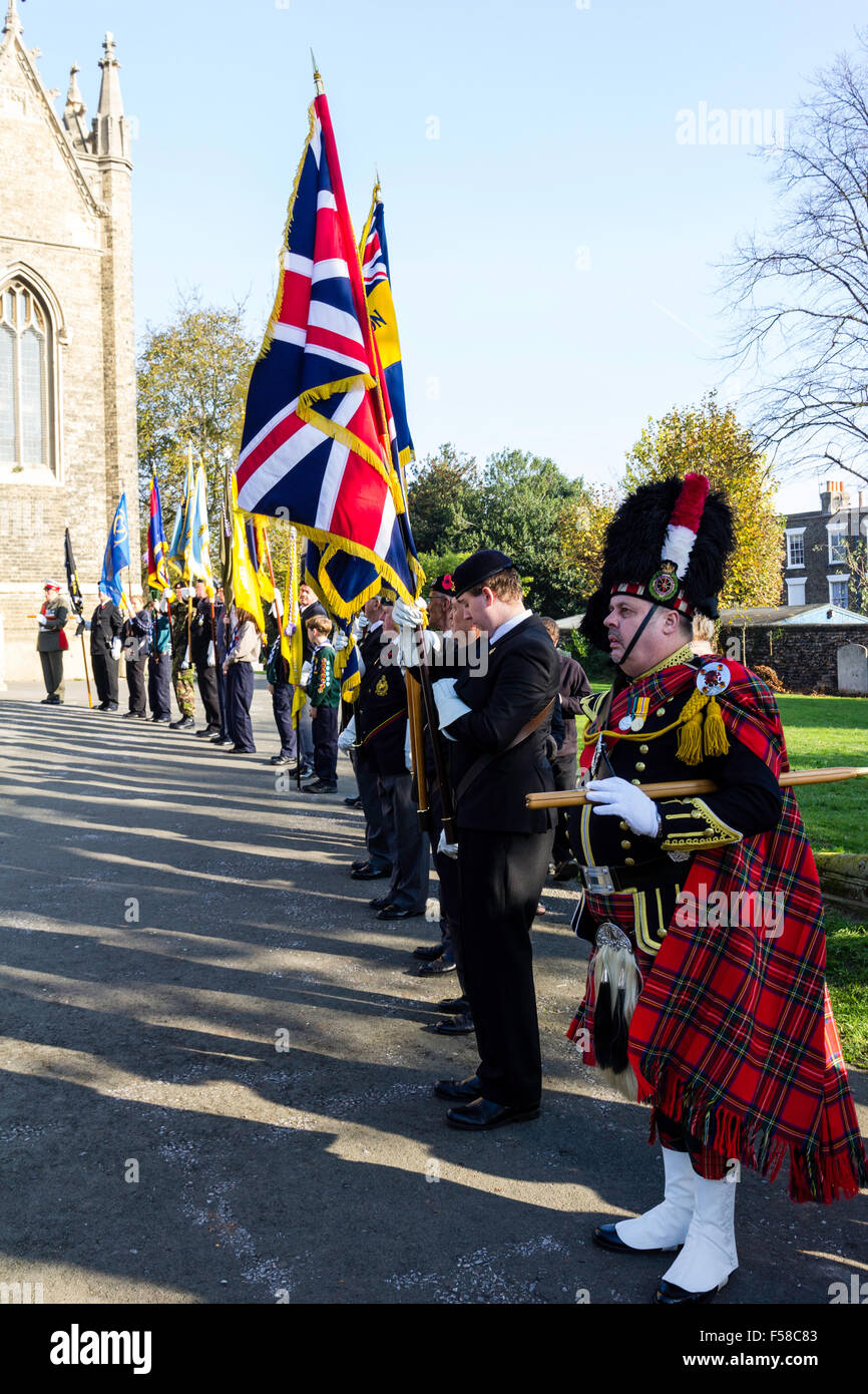 England, Ramsgate. Remembrance Sunday. Row of ex-servicemen standing at attention with flags and standards in front of church. Highlander leading. Stock Photo