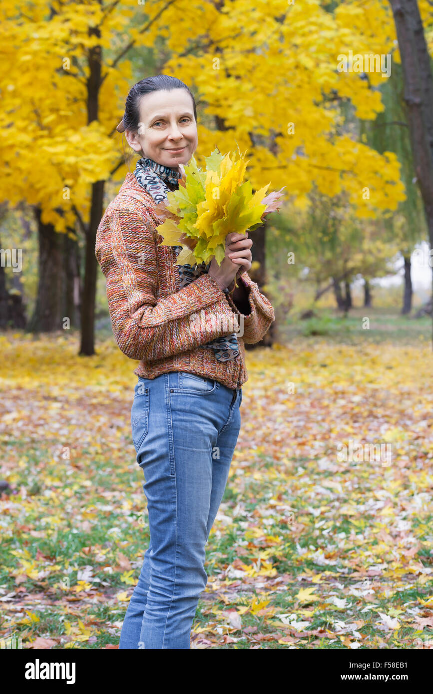 A smiling adult caucasian woman is picking yellow maple leaves in ...