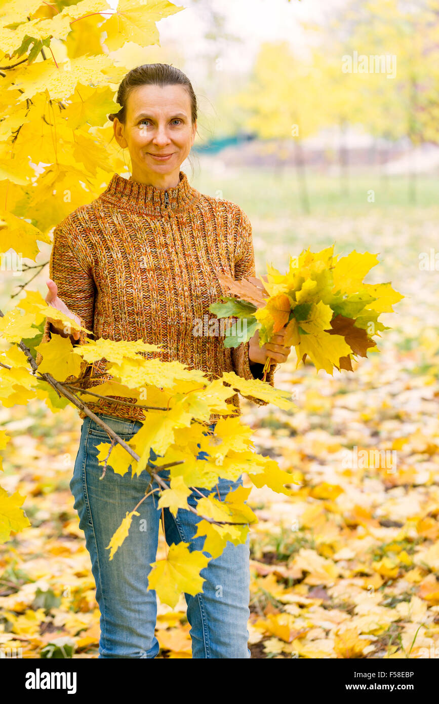 A smiling adult caucasian woman is picking yellow maple leaves in ...