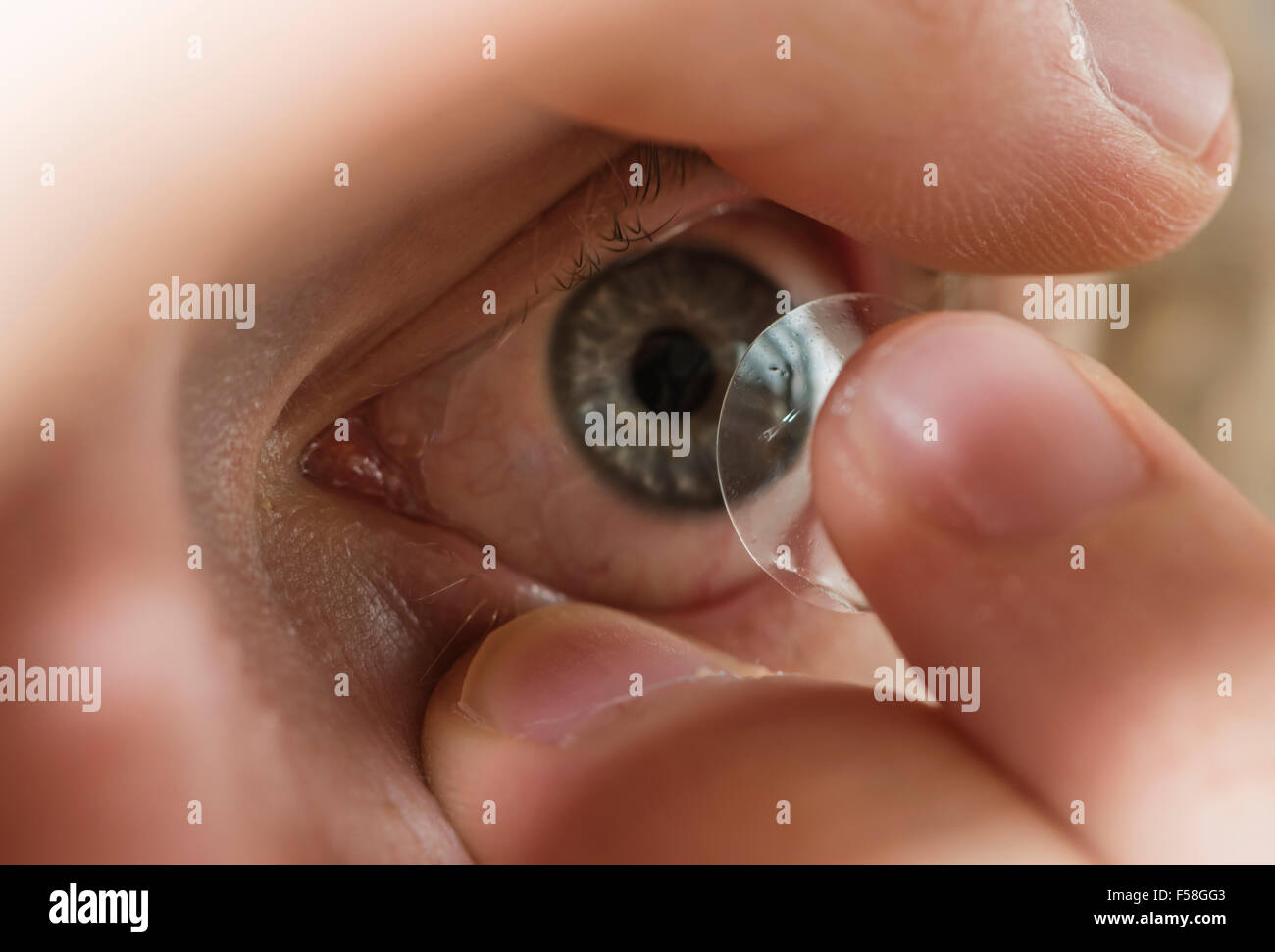 A man is inserting a contact lens into his left eye. Stock Photo