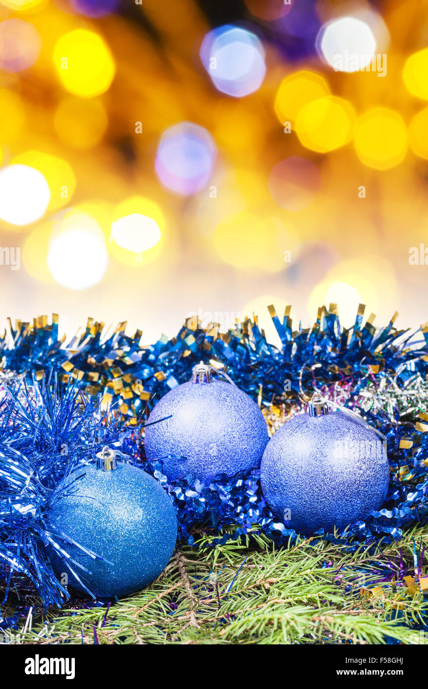 Xmas still life blue balls, tinsel at green tree with blurred yellow and violet Christmas
