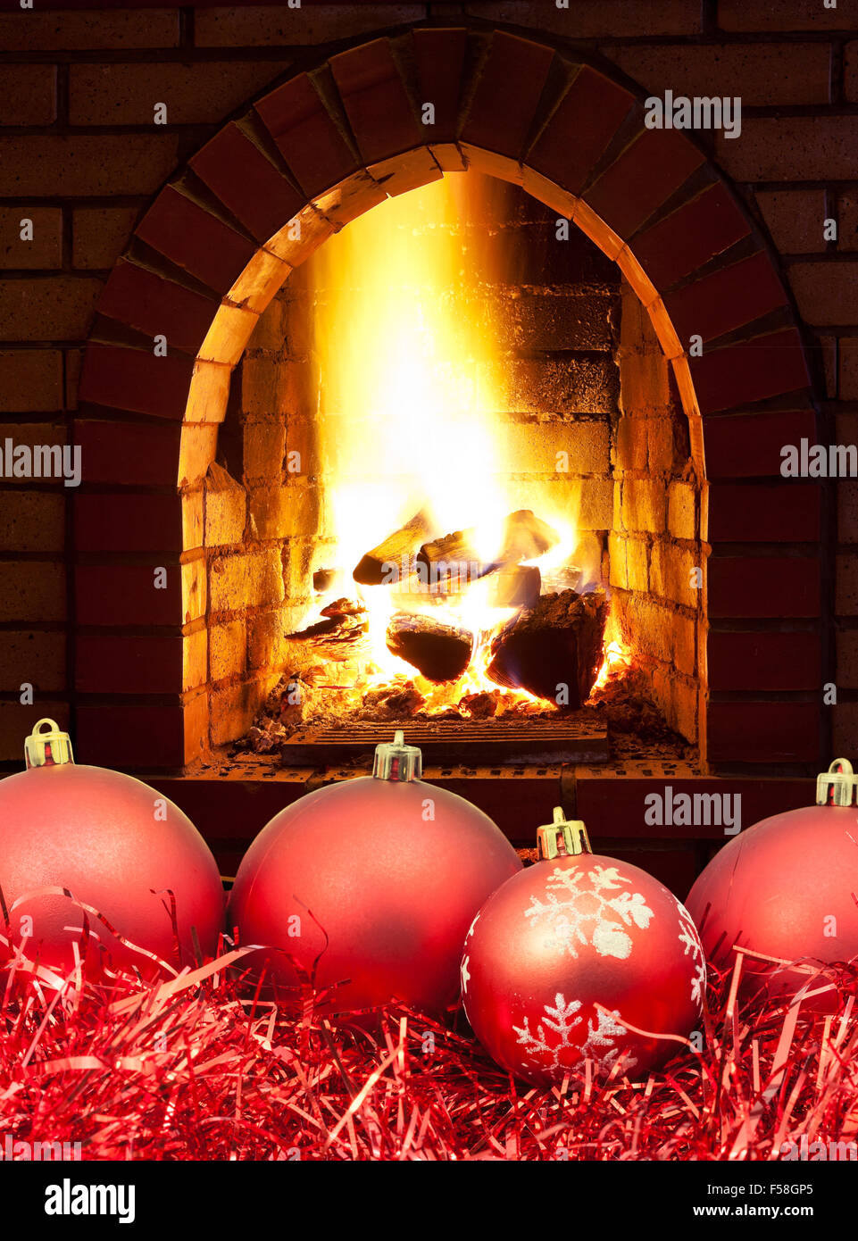 red Christmas balls and tinsel with open fire in home fireplace Stock Photo