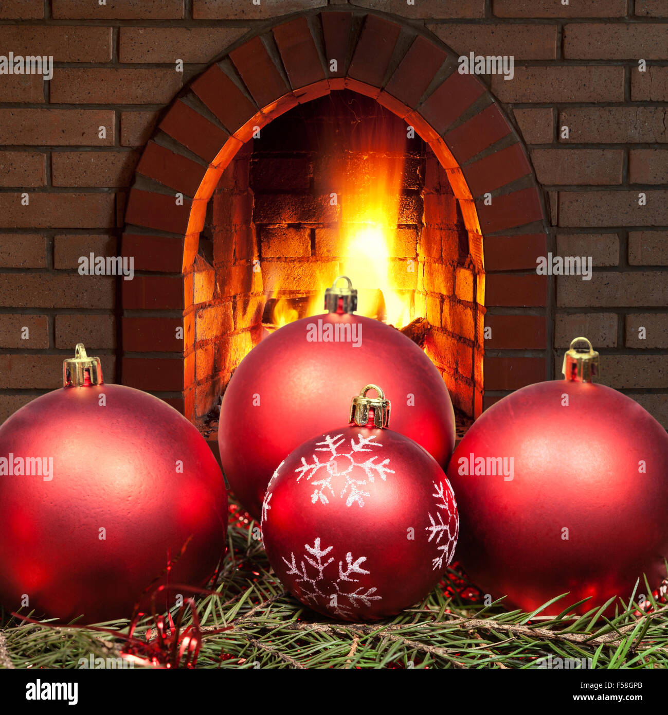 red Xmas baubles on green spruce tree with open fire in home fireplace Stock Photo