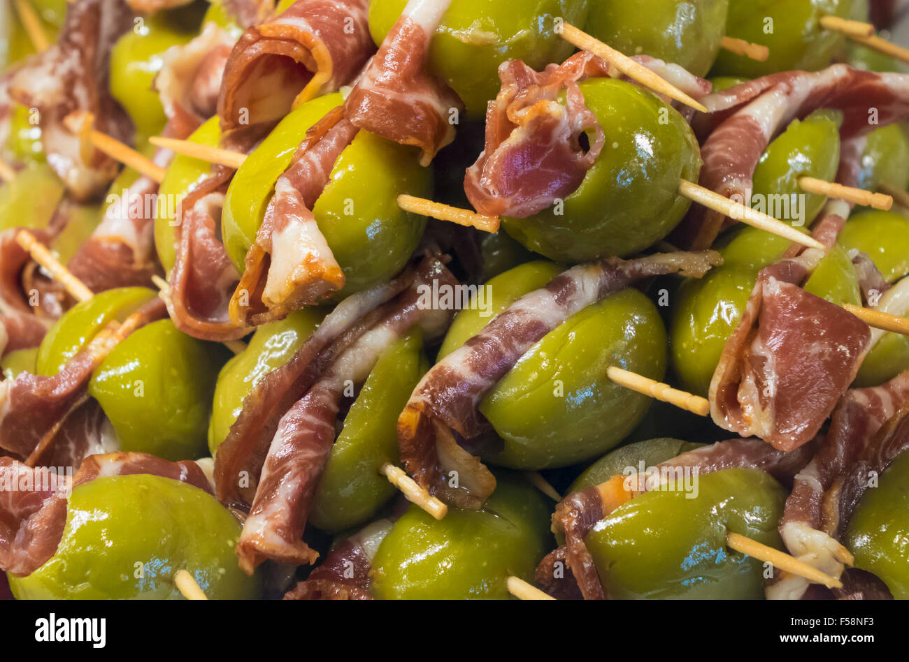 Green olives and Iberian ham or bacon on plate of hors-d'oeuvres or entradas in food counter in Spanish market in Madrid Stock Photo
