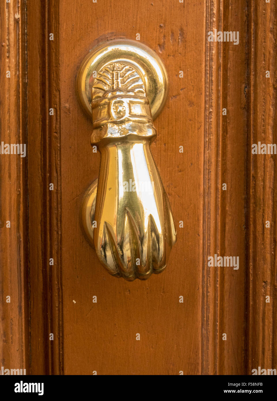 Front view of brass door knocker shaped like a hand on old wooden door Stock Photo