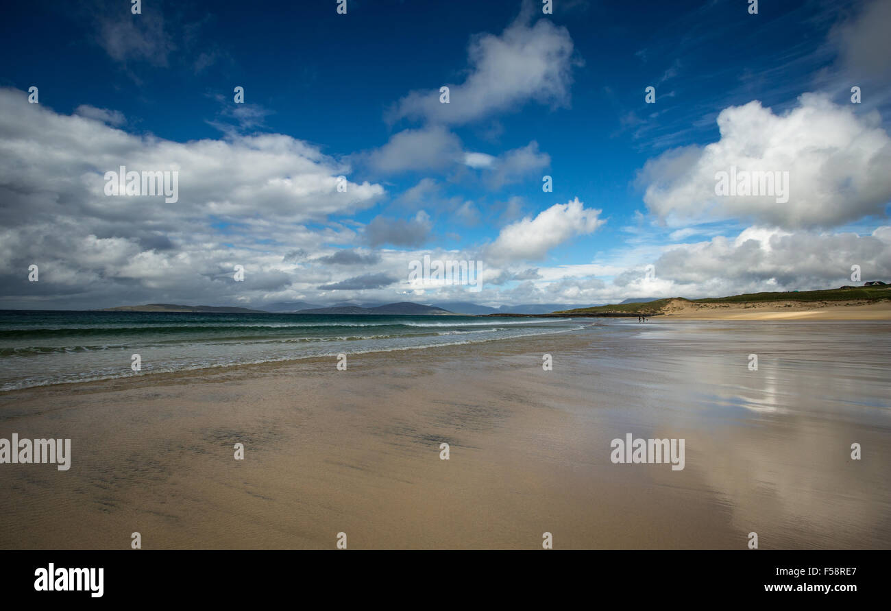 two distant figures walk under the blue sky and summer clouds over the wet sand and receding tide at Scarista Beach, Outer Hebrides, Scotland Stock Photo