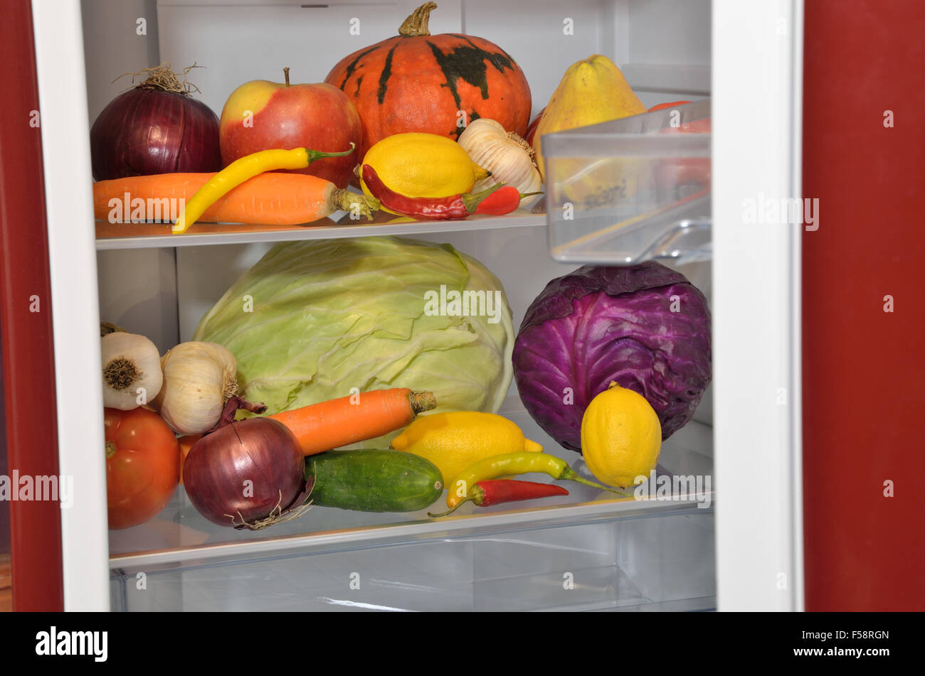 Fresh fruits and vegetables on shelves of half-opened refrigerator Stock Photo