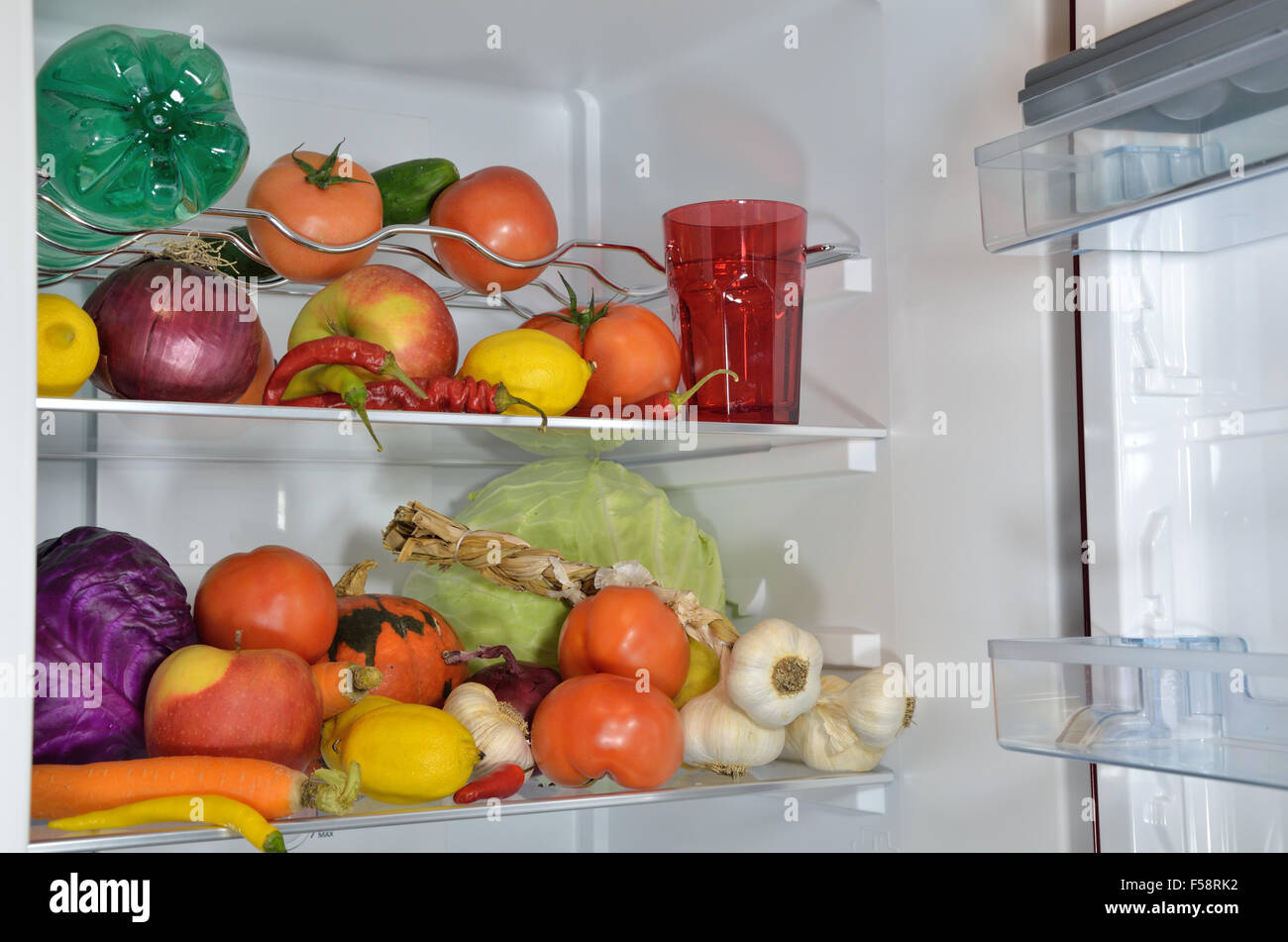 Different fruits, vegetables and water on refrigerator shelves Stock