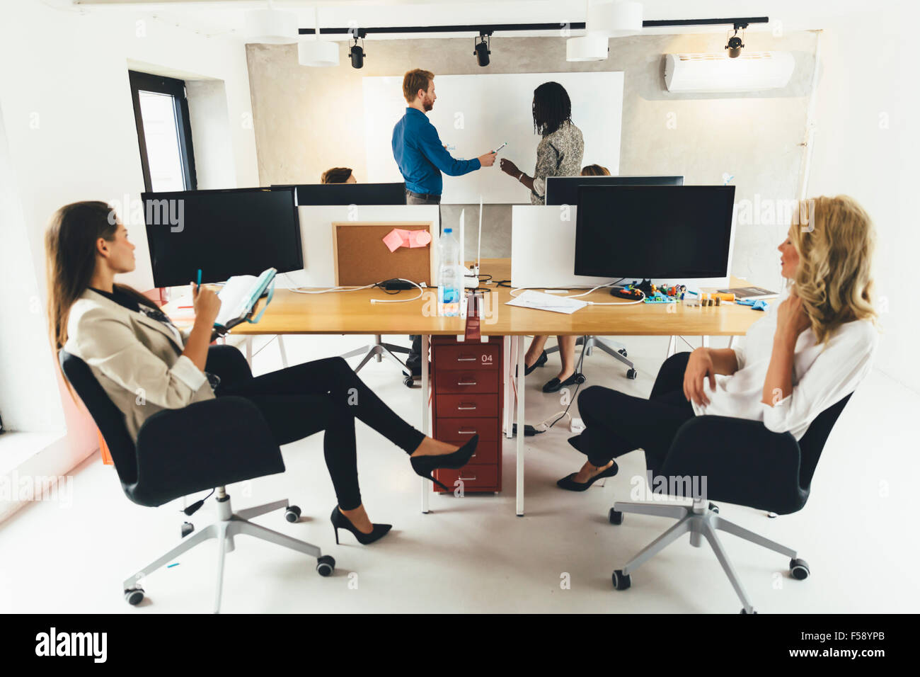Young business people sitting in office while listening to the lecturer and learning new technologies displayed on the whiteboar Stock Photo