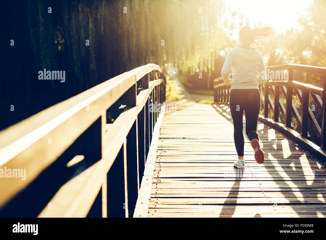 Beautiful female jogger running during sunset across bridge Stock Photo