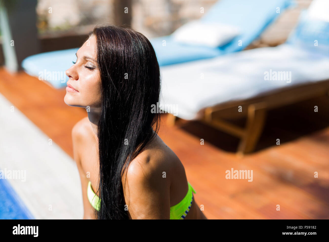 Beautiful woman with closed eyes sunbathing at the poolside Stock Photo