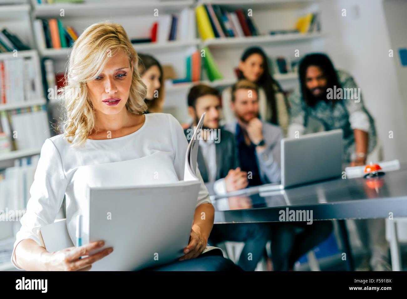 Beautiful woman reading a document while  her employees are solving problems in the background Stock Photo