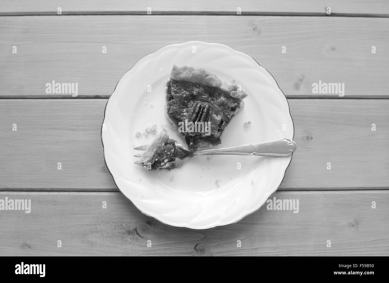Half-eaten slice of pecan pie on a china plate with a dessert fork - monochrome processing Stock Photo