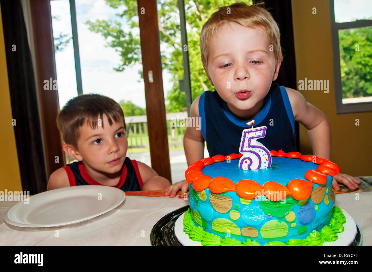 Boy blows out birthday candle on cake Stock Photo