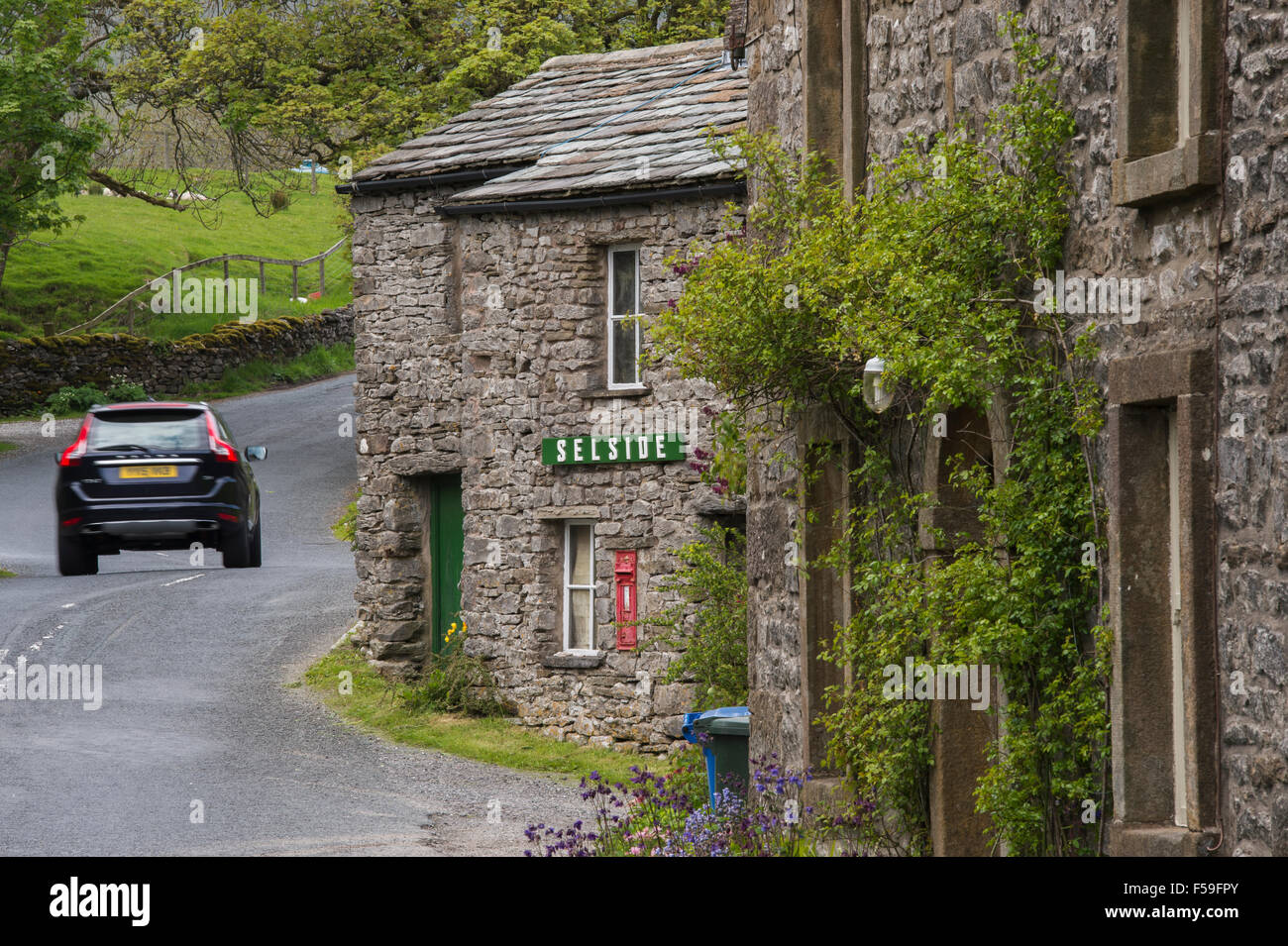 Car passes traditional, stone-built, roadside cottages  (name sign & post box) - quaint hamlet of Selside, Yorkshire Dales National Park England UK. Stock Photo