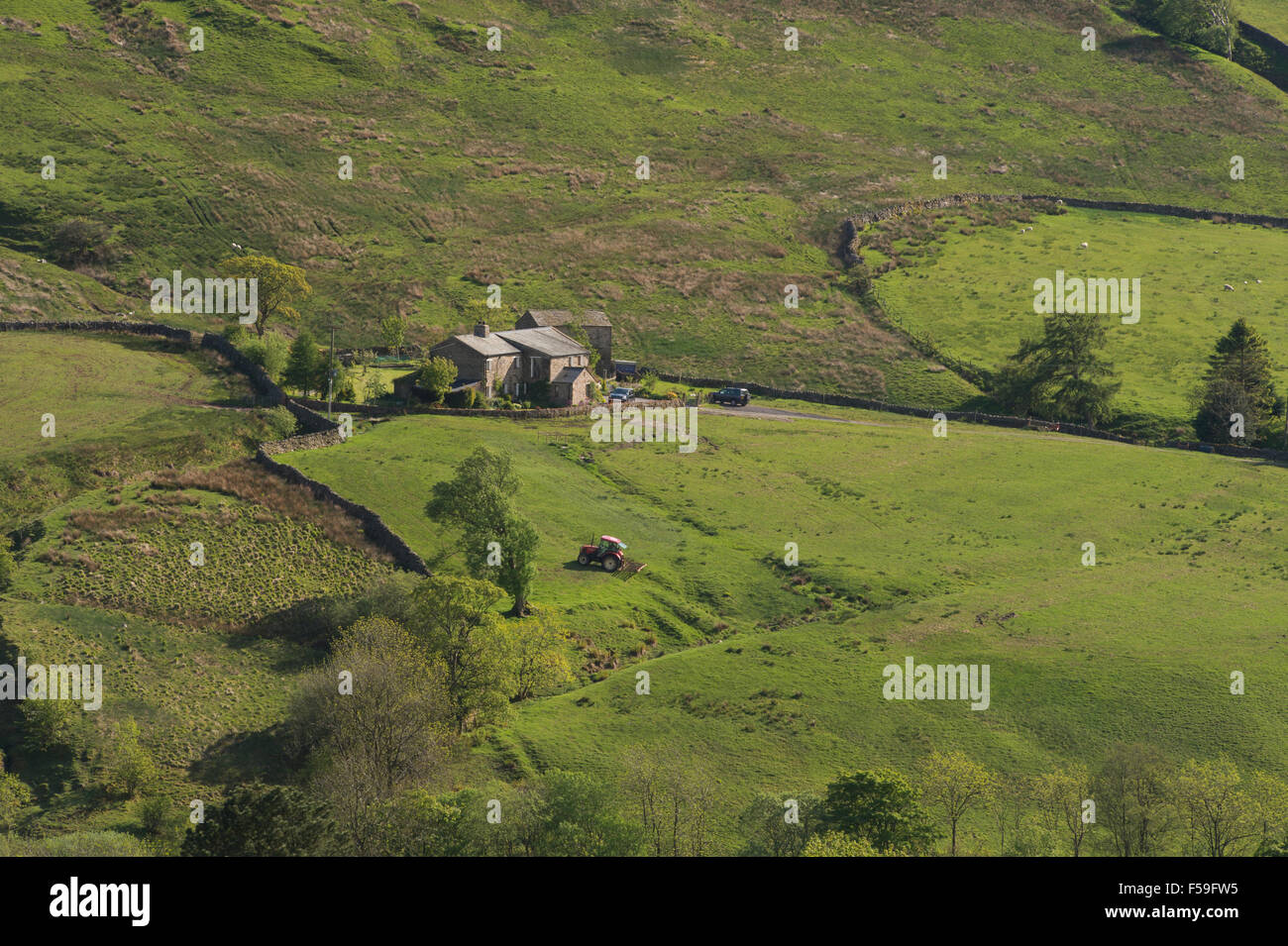 Sunny, high view over the fells in the valley of Dentdale, Cumbria, England, UK - isolated farm & tractor working in a field on steep-sided hillside. Stock Photo