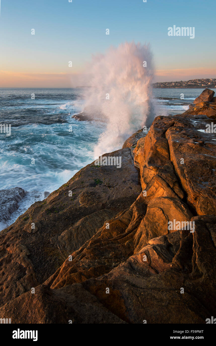 Sunrise seascape with unrest sea and blue water and with sky lit orange rocks and big crashing wave Stock Photo