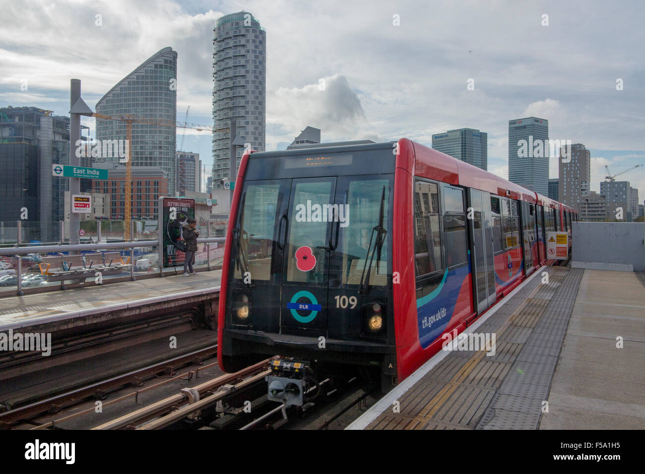 A red Docklands Light Railway (DLR) train wearing a poppy approaches East India DLR Station, London, England, United Kingdom Stock Photo