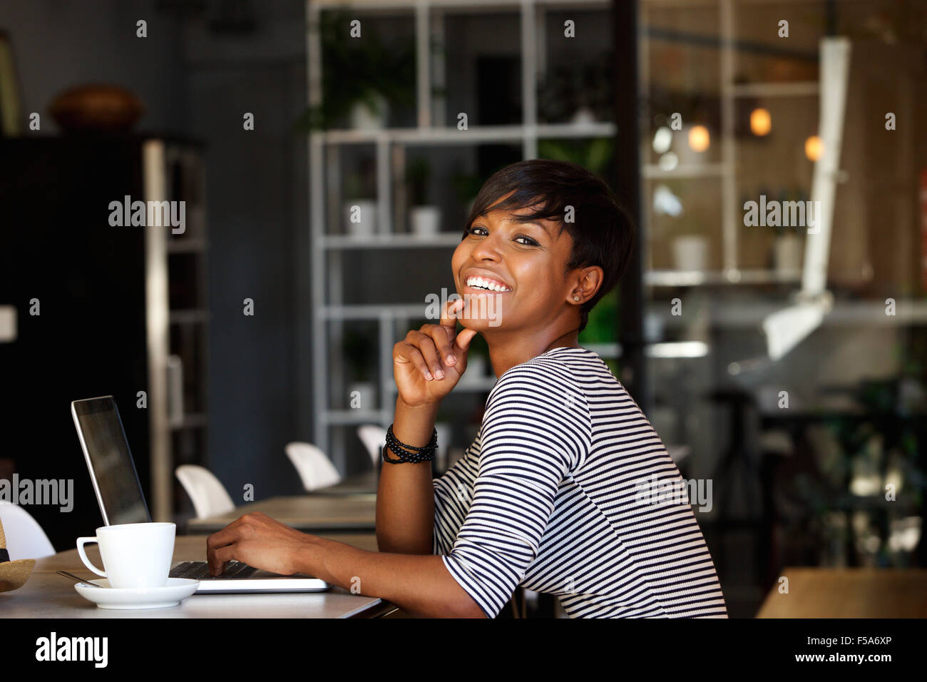 Side portrait of a smiling young african american woman sitting at cafe ...
