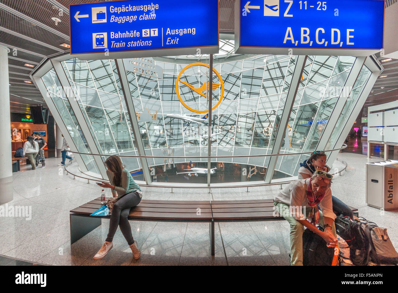Frankfurt, Germany. People waiting in the Airport. Large 'Lufthansa' logo in the background. Stock Photo