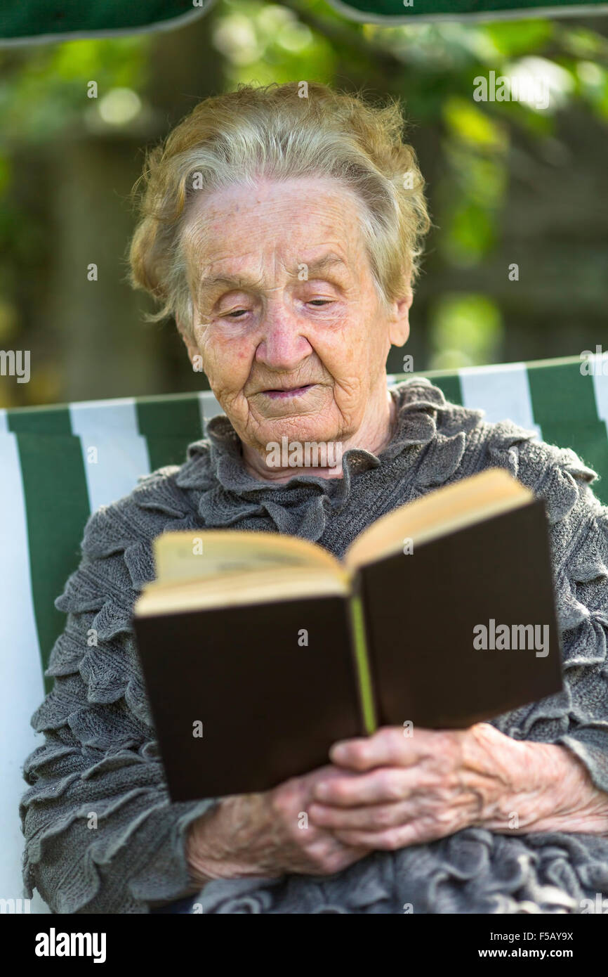 Senior woman reading a book sitting in the garden Stock Photo - Alamy