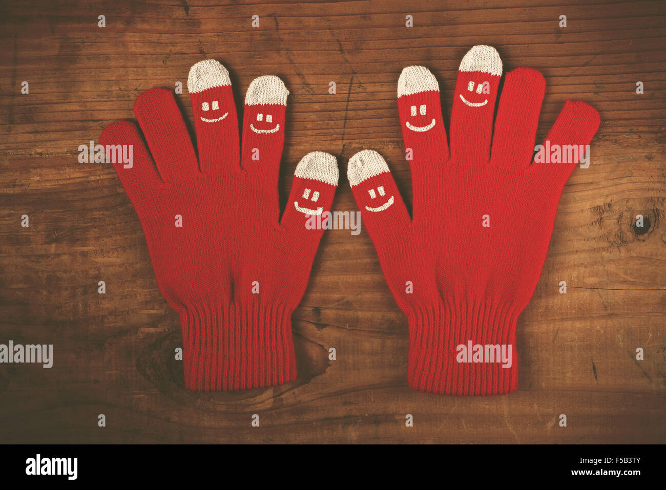 Christmas winter wool gloves with smiley emoticons on wooden desk, top view, retro filter toned image Stock Photo