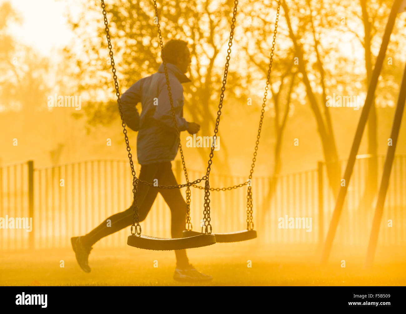 Mature Man Jogging Past Swing In Public Park On A Mist