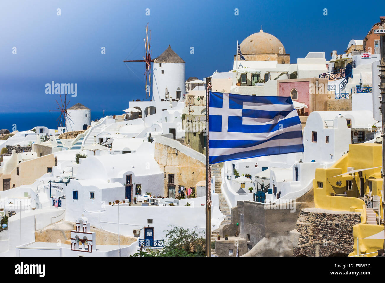 Blue sky and flag near traditional white village on island of Santorini, Greece Stock Photo