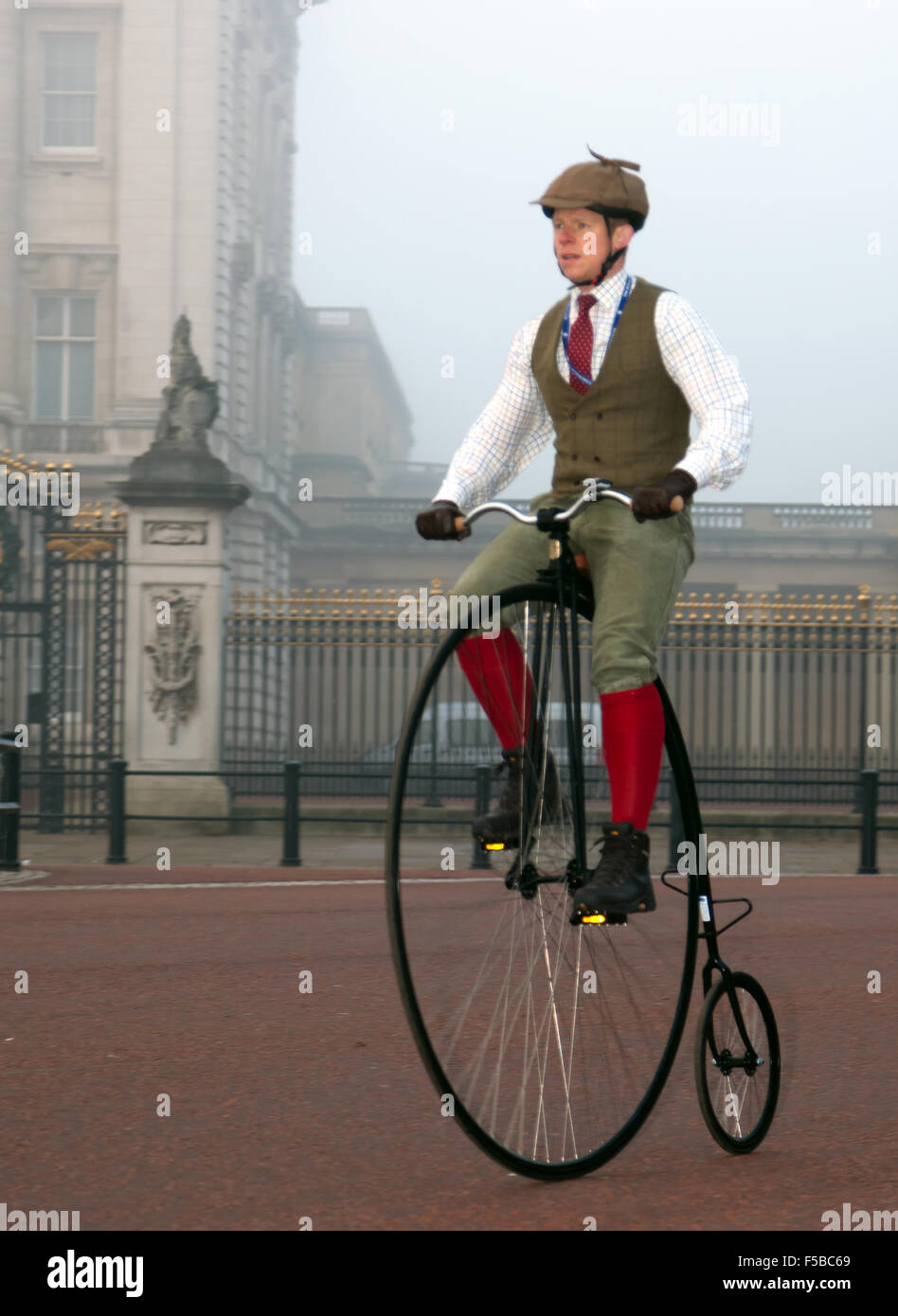 A man, in period costume cycles past Buckingham Palce, on an old Penny-farthing, during the London to Brighton veteran Car Run. Stock Photo