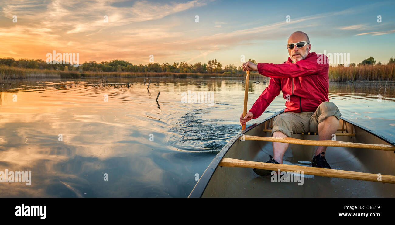 senior paddler enjoying paddling a canoe on a calm lake at sunset, Riverbend Ponds Natural Area, Fort Collins, Colorado Stock Photo