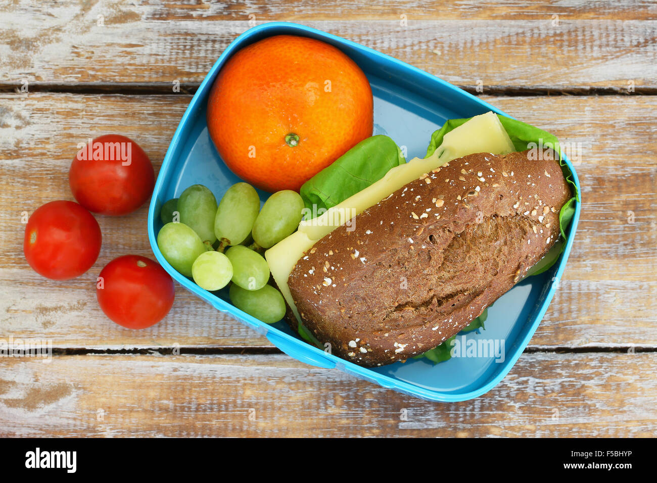Healthy school lunch box containing brown cheese roll, mandarine