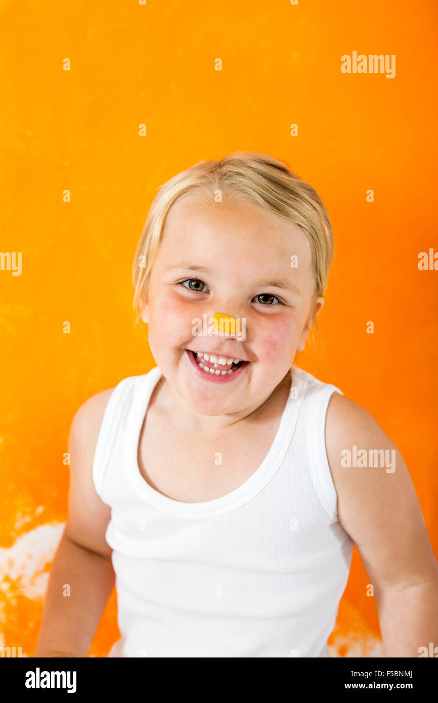 Little girl painting white wall with orange color. She´s got orange paint on her little nose. Stock Photo
