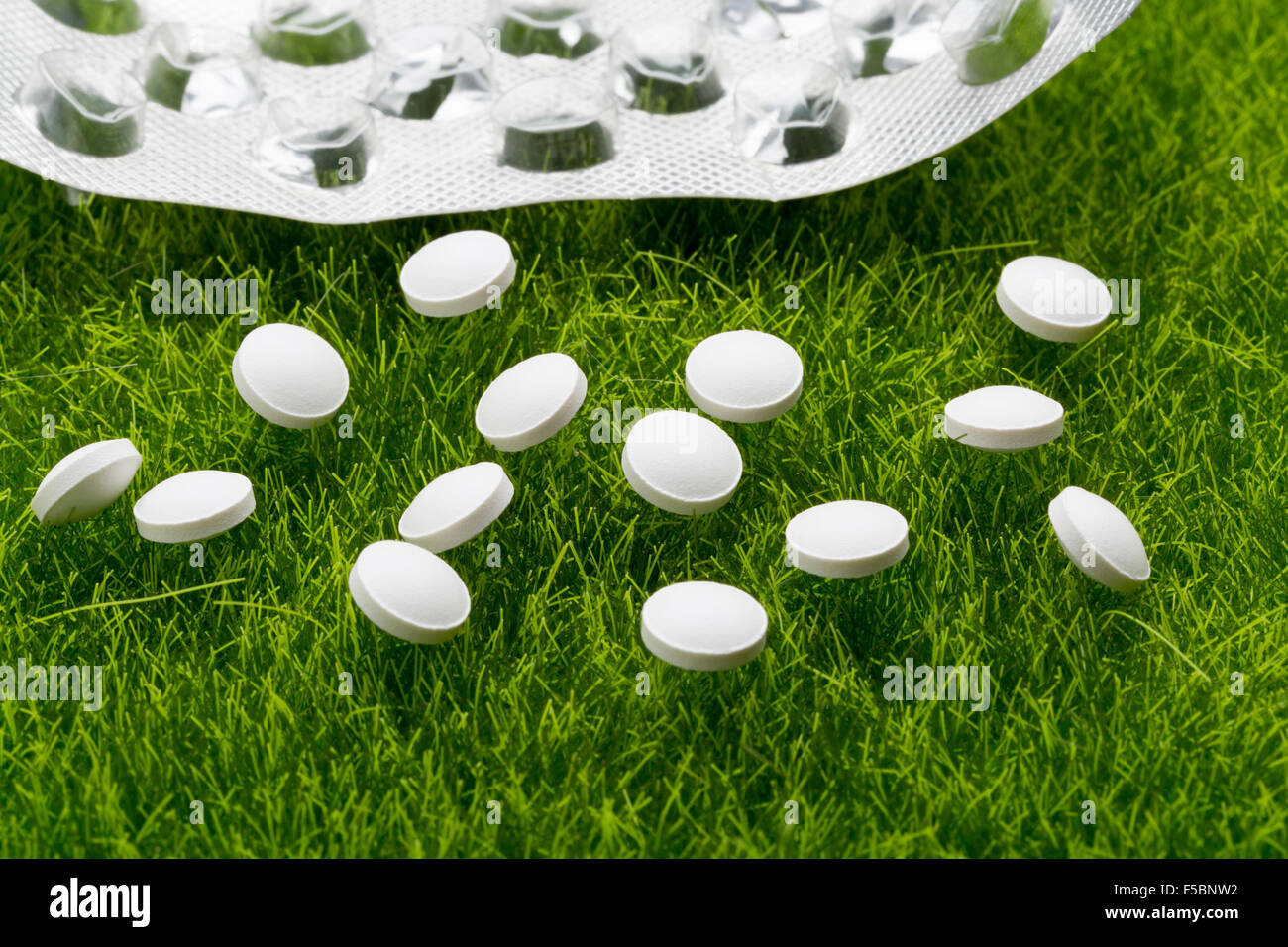 White antibiotic pills and empty blister pack scattered on the green grass Stock Photo