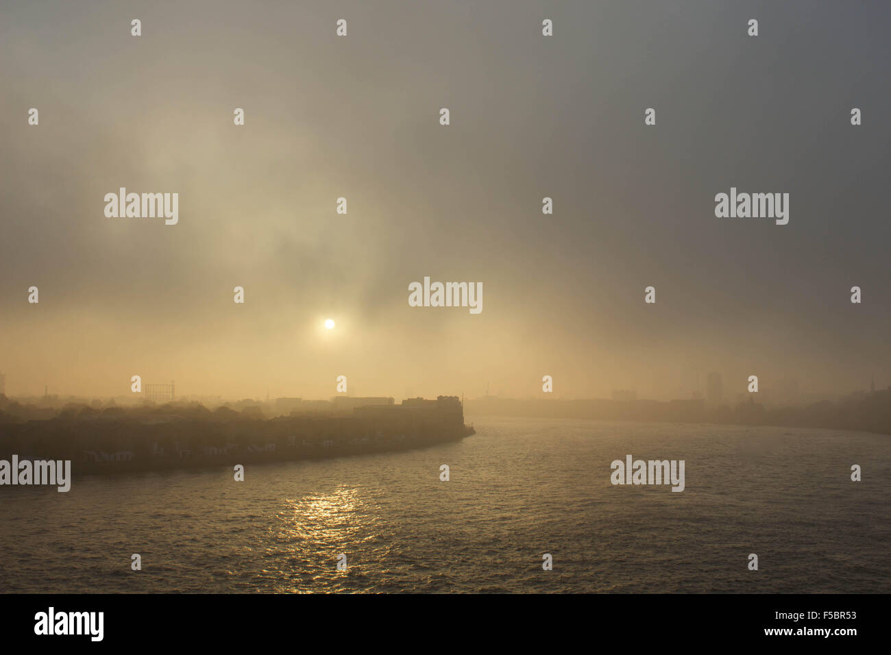London, UK.  1st November 2015. A thick fog rolls in again from the east to cover The Docklands and hide its landmark skyscrapers. Mist continues east over Rotherhithe, making for an eeir sunset over the River Thames. 1st November 2015. Credit:  Glenn Sontag / Alamy Live News Stock Photo