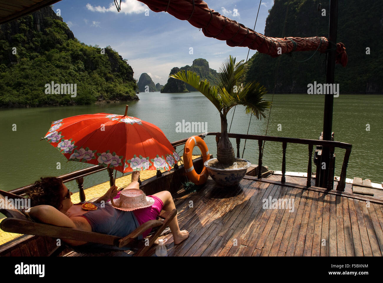 Tourists relaxing inside a Chinese Junk, Halong Bay Tourist Boat Tour, Vietnam. Junk, boat sailing amongst karst limestone mount Stock Photo