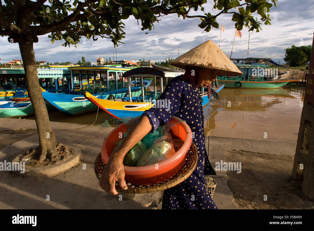 Traditional boats on the Song Thu Bon river, Hoi An, Vietnam, Southeast Asia. Woman with a traditional hat passing in front of t Stock Photo