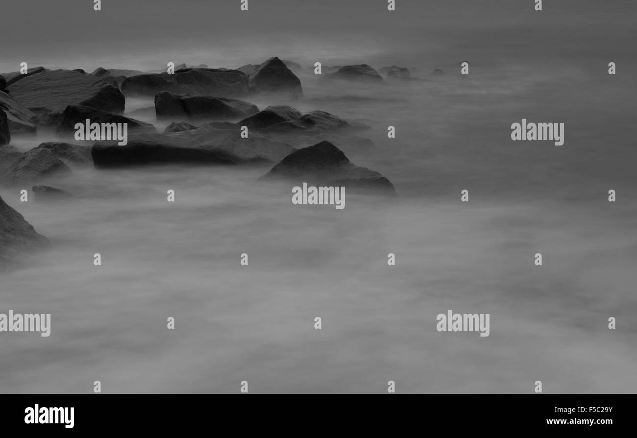 eerie misty foreground of waves surrounding large rocks in the sea Stock Photo