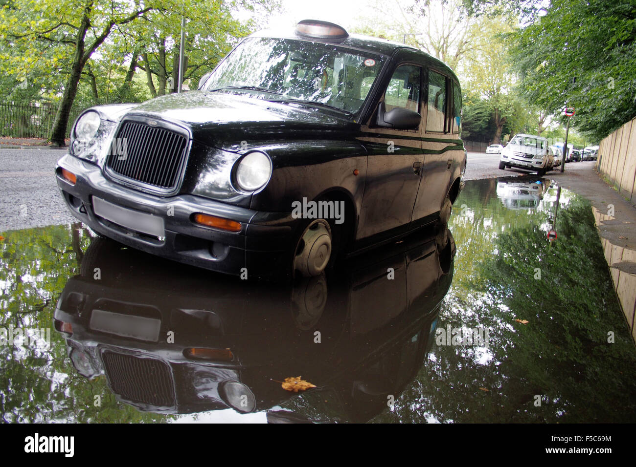 black cab taxi in puddle or rain water on london road england uk Stock Photo