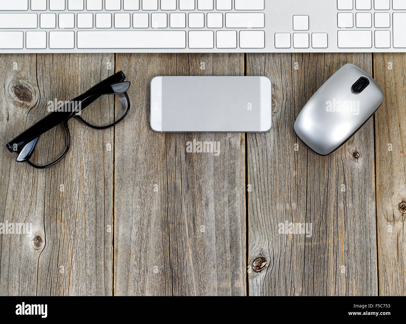 Office wooden desktop, boards running vertically, with computer keyboard, mouse and reading
