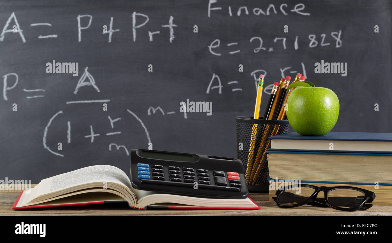 Student desk, for finance course, in front of chalkboard with financial formulas. Stock Photo