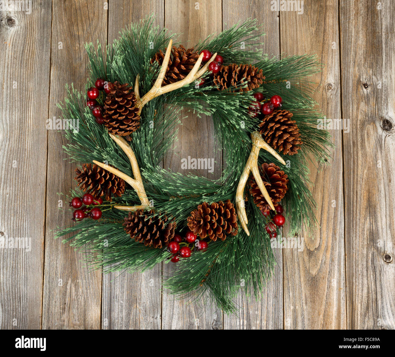 Western style wreath with antlers, pine cones and berries on rustic wood. Boards in vertical layout. Stock Photo