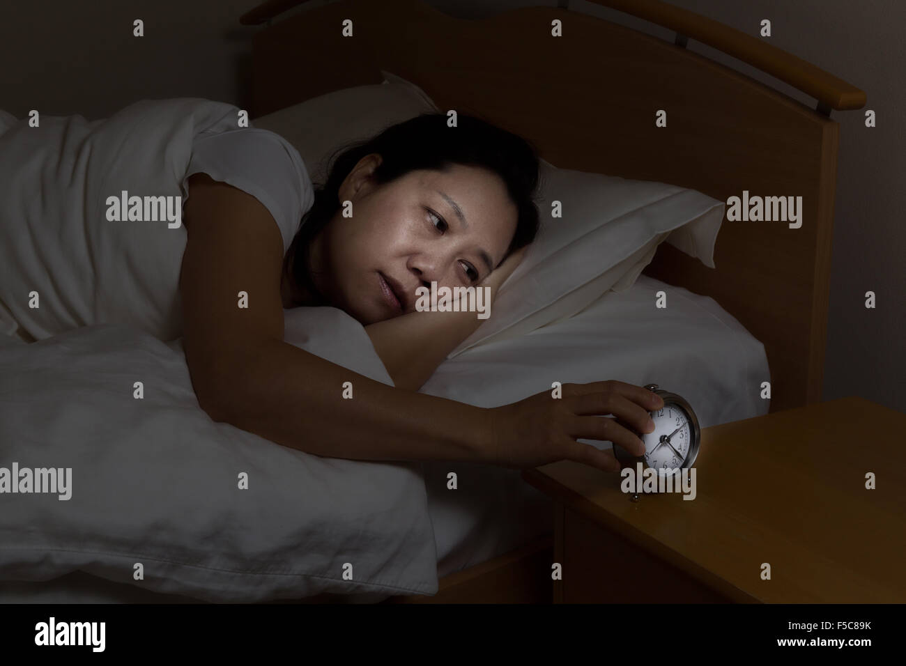 Woman with insomnia touching alarm clock while eyes open. Select light