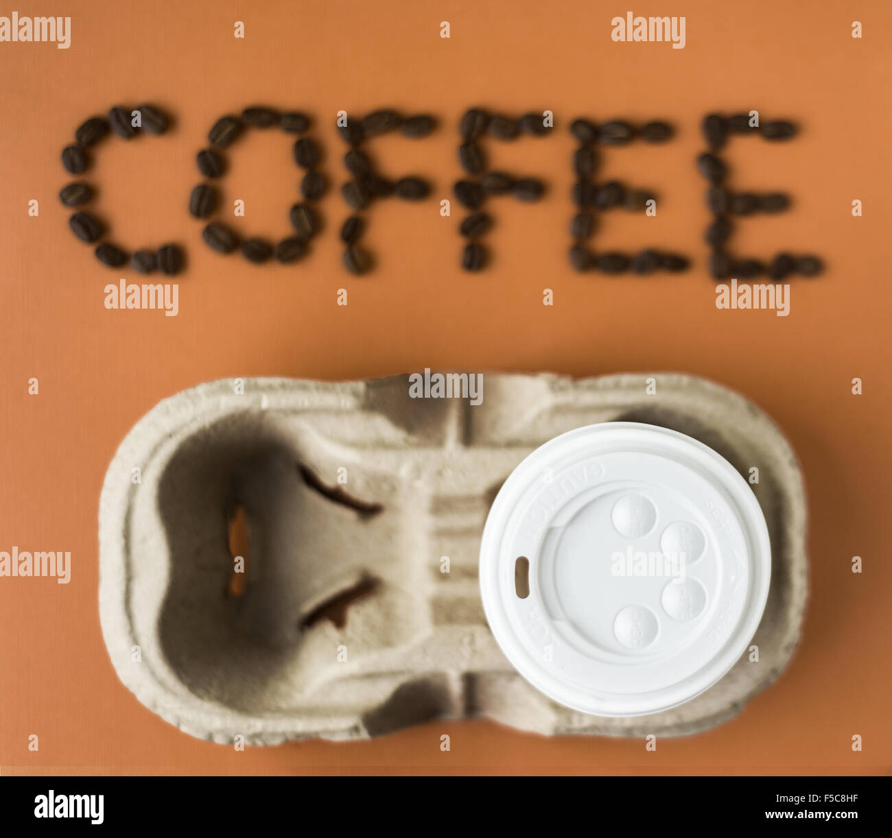 takeaway coffee cup with 'coffee' spelt out in beans, blurred, on an orange background Stock Photo