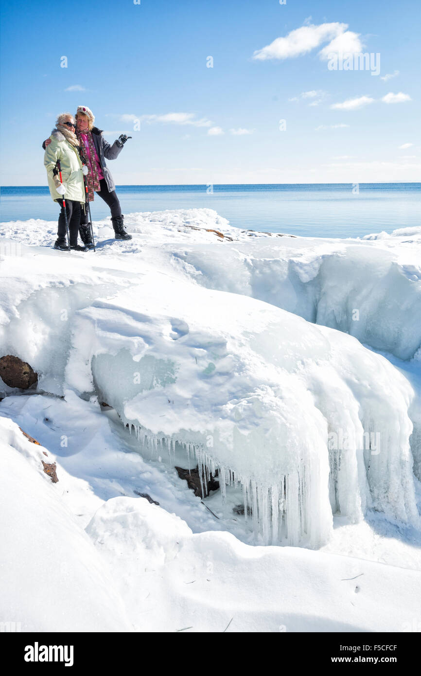 Two adult women explore a treacherous icy snowbank on the frozen shore of Lake Superior in winter, Two Harbors, MN, USA Stock Photo