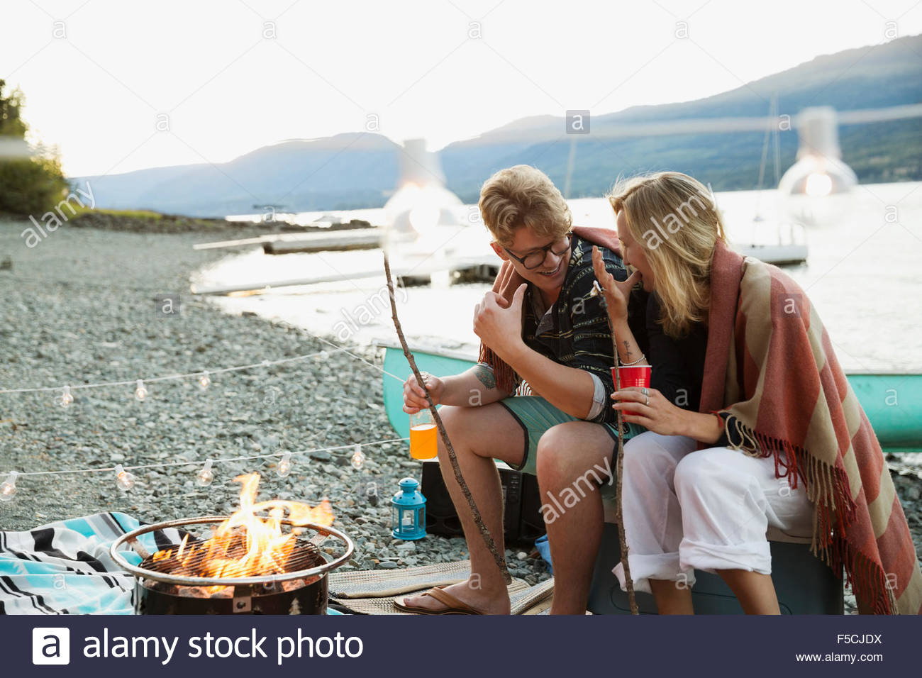 Young couple roasting marshmallows at lakeside campfire Stock Photo