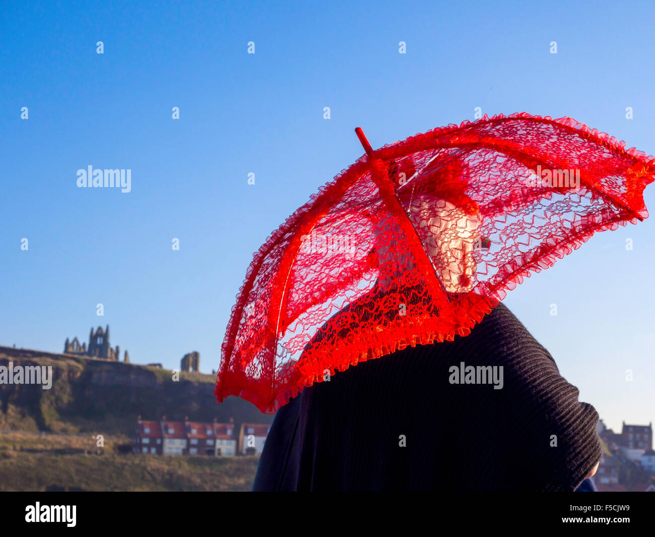 A woman in Victorian dress  using a red parasol walking in the sunshine on the West Pier at Whitby Goth Week End November 2015 Stock Photo