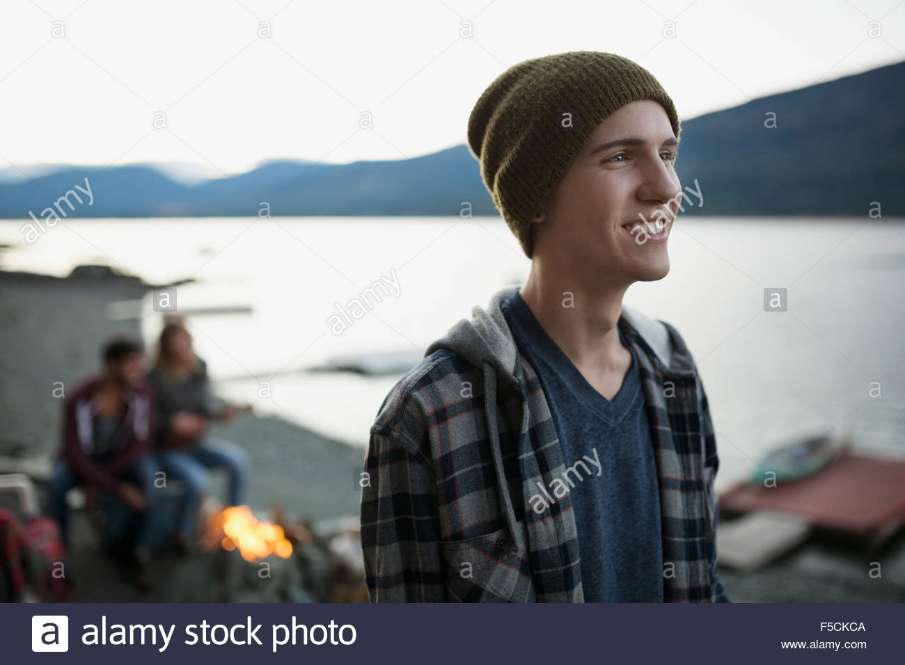 Smiling young man at lakeside near campfire Stock Photo