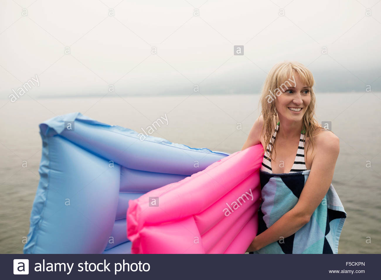 Smiling woman carrying pool rafts in lake Stock Photo