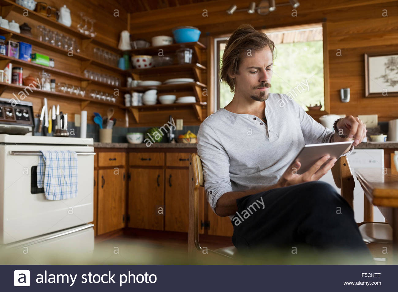Man using digital tablet at cabin kitchen table Stock Photo